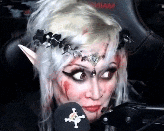 a woman with blood on her face is sitting in front of a microphone wearing elf ears and a crown .