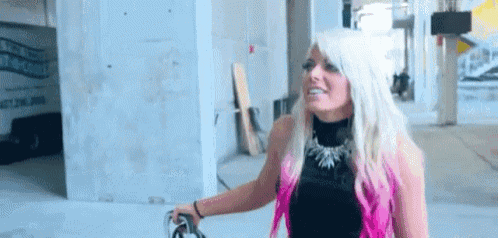 a woman with blonde hair and pink streaks is standing in a building holding a pair of scissors .