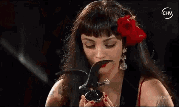 a woman with a red rose in her hair is holding a pair of scissors .