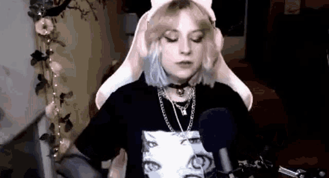 a girl is sitting in front of a microphone wearing a cat hat and a black shirt .