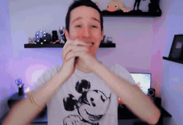 a man wearing a mickey mouse shirt is clapping his hands together