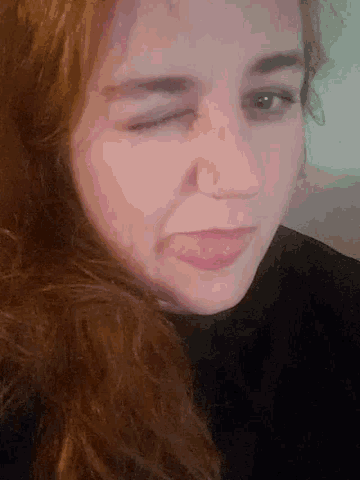 a woman with long red hair is making a funny face with her eyes closed .