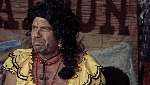 a man in a wig is sitting in front of a sign that says ' a ' on it