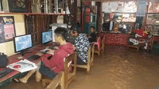 a group of people are sitting at desks in a flooded room playing computer games .