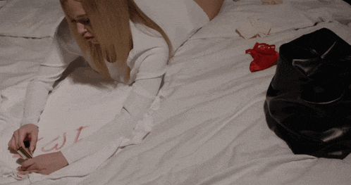 a woman is laying on a bed writing on a piece of paper with red paint