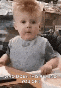 a baby is sitting at a table wearing a bib and making a face .