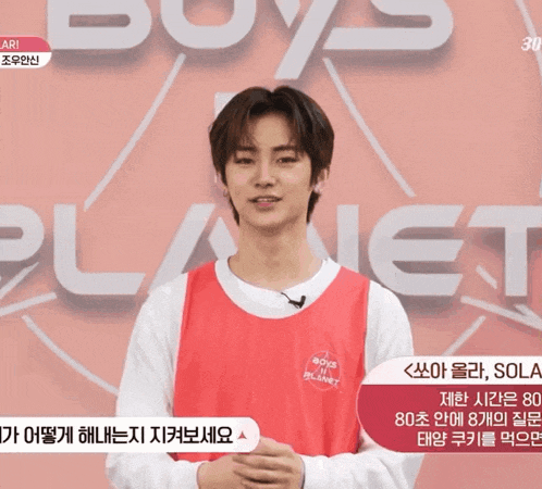 a young man stands in front of a sign that says " boys planet "