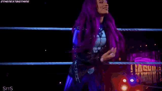 a woman with purple hair is standing in a wrestling ring with a crowd behind her .