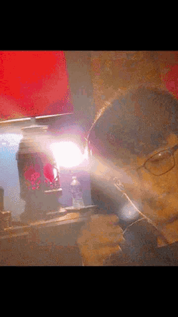 a man with glasses is holding a flashlight in front of a red wall