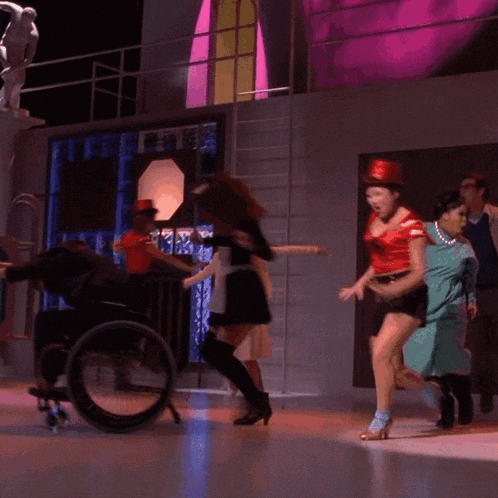 a woman in a red top hat is dancing on a stage with other women
