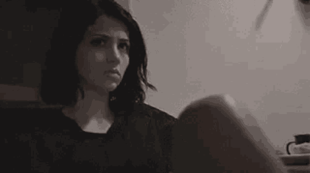 a woman in a black shirt is sitting at a table in a dark room .