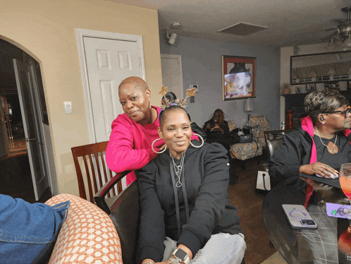a woman in a pink shirt is putting a ponytail on a woman in a black hoodie