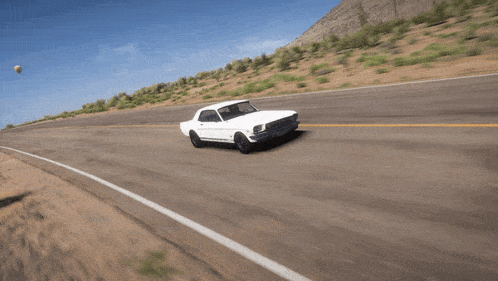 a white car is driving down a road with a mountain in the background
