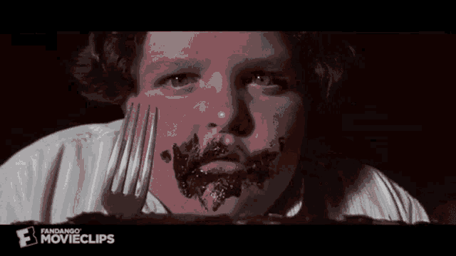 a boy with chocolate on his face is holding a fork in front of his mouth .