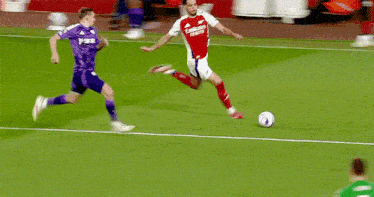 a soccer player wearing a red emirates jersey is kicking the ball