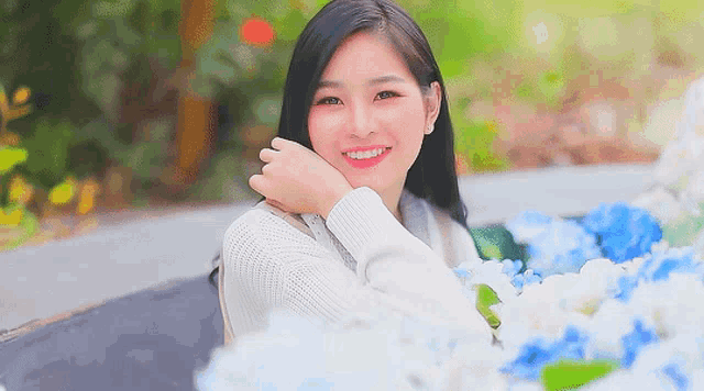 a woman in a white sweater is smiling in front of a bunch of blue and white flowers