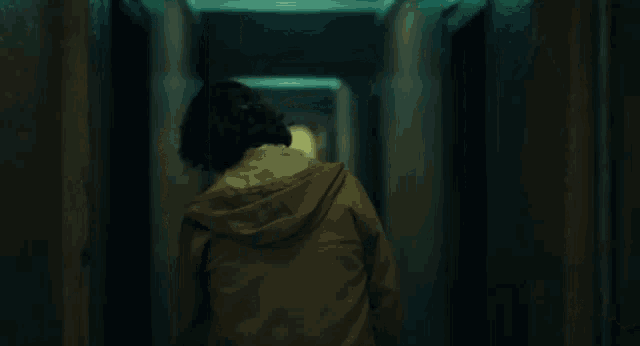 a person is walking down a dark hallway with a hood on .