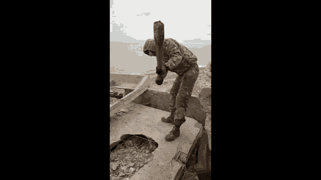 a man in a military uniform is standing on top of a concrete wall holding a hammer .
