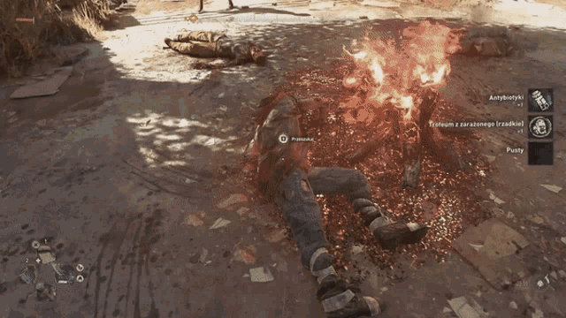 a video game is being played and a person is laying on the ground with a fire in the background