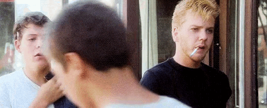 a man is smoking a cigarette in front of a window while two other men look on .