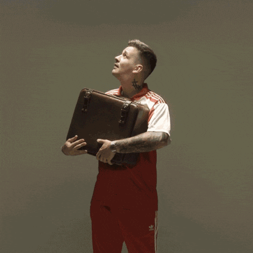 a man in a red and white adidas shirt holds a suitcase