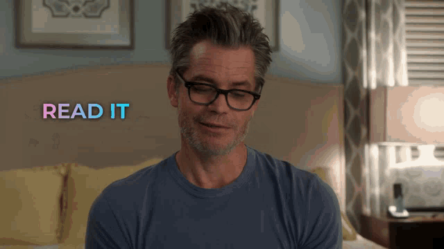 a man wearing glasses is sitting in front of a bed and the words read it are above him