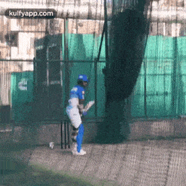 a cricket player is swinging a bat at a ball in a cage .