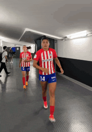 a woman in a red and white striped shirt with the number 14 on her shorts walks down a hallway