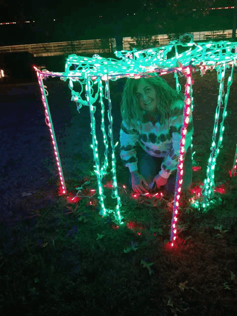 a woman is kneeling down in front of a christmas light display