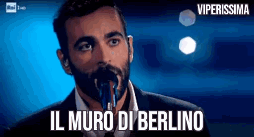 a man singing into a microphone with the words il muro di berlino written below him