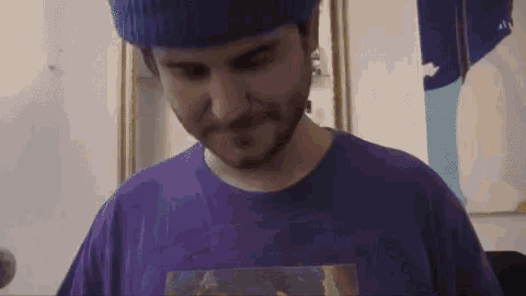 a man wearing a blue beanie and a purple shirt is looking down .