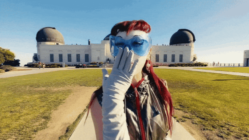 a woman wearing blue glasses and white gloves covering her face in front of a building