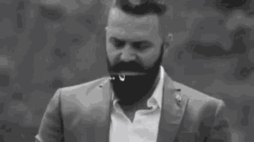 a black and white photo of a man with a beard wearing a suit .