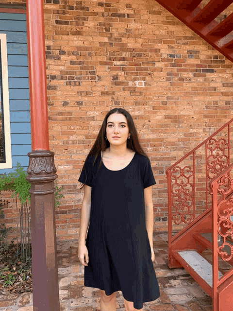 a woman in a black dress is standing in front of a brick building