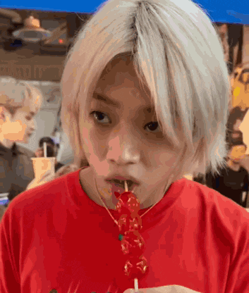 a young man with white hair is eating a red candy on a stick .