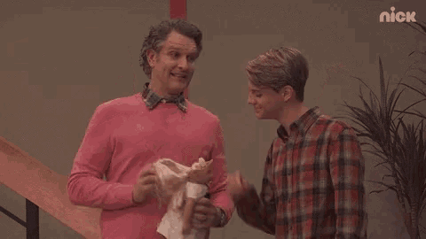 a man in a pink sweater is holding a doll next to another man