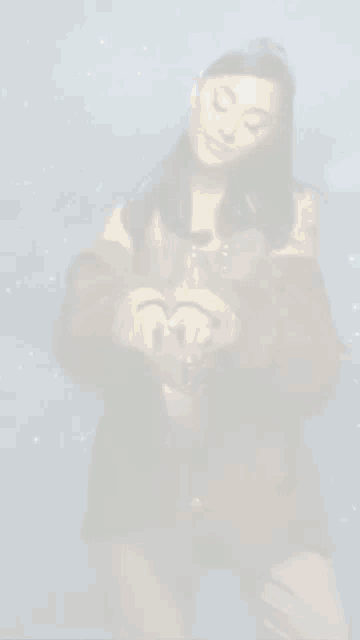ariana grande is making a heart shape with her hands while standing in front of a starry sky .
