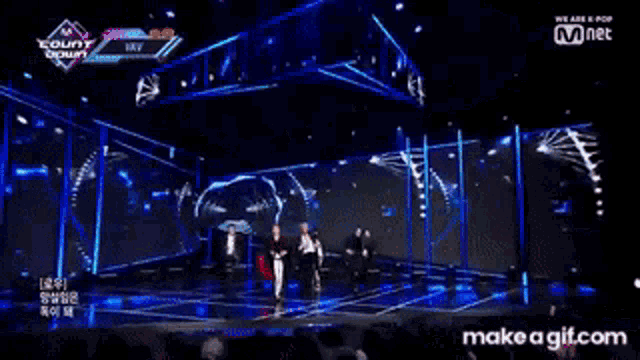 a group of people are dancing on a stage in front of a large screen that says mnet .