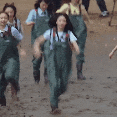 a group of women wearing overalls are running through the mud .
