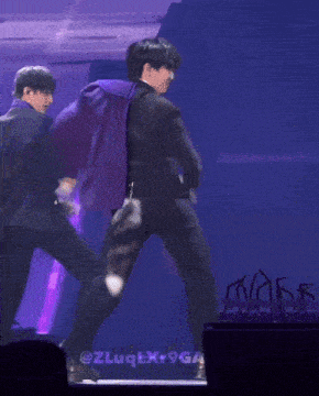 a man in a black suit is dancing on a stage with a purple background