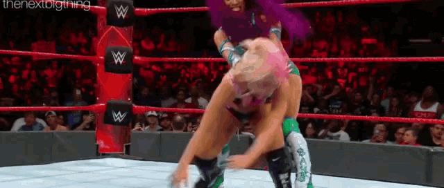 a woman is wrestling another woman in a wrestling ring with a crowd watching .
