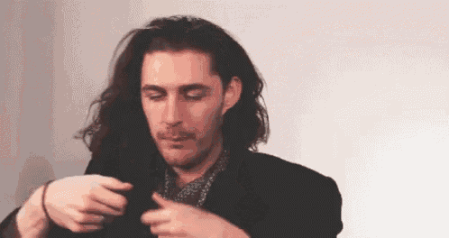 a man with long hair and a beard is wearing a black jacket and a tie .