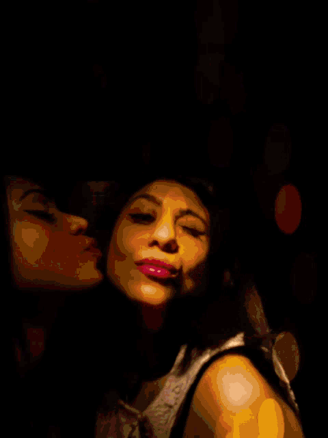 two women are kissing each other on the cheek in a dark room