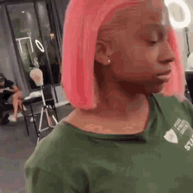 a woman with pink hair is wearing a green shirt and standing in a salon .