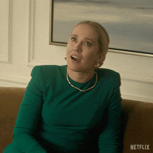 a woman in a green dress is sitting on a couch with netflix written on the bottom right