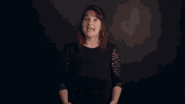a woman in a black dress is speaking in a foreign language