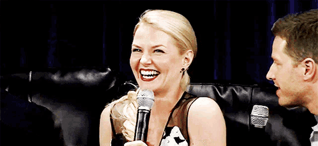 a woman is laughing while holding a microphone in front of a man