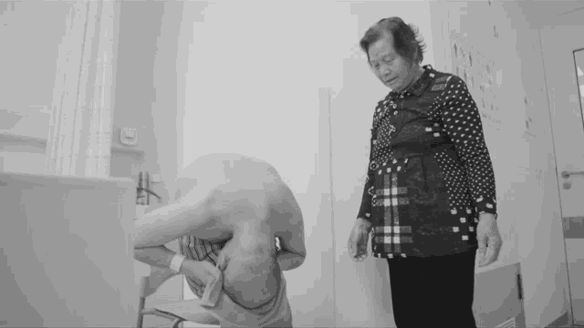 a black and white photo of a woman standing next to a man in a hospital room