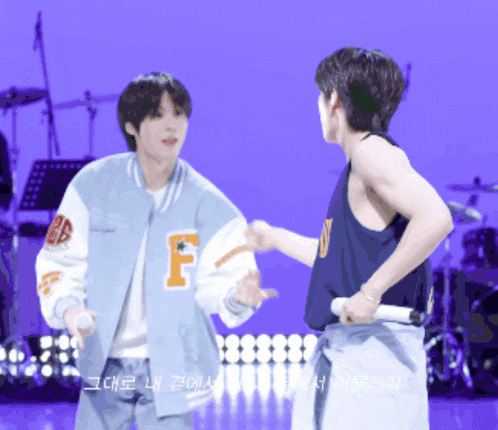 a man wearing a jacket with the letter f on it stands next to another man
