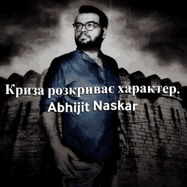 a man with glasses and a beard is standing in front of a brick wall with the name abhijit naskar written on it